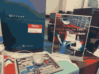 a blue computer (silicon graphics OCTANE) with a hello my name is badge introducing the machine as wilson :) next to a poster reading, check out the 1997 VRML tradeshow, with a low-poly monoral and guy in a hat next to a virtual computer display and powerpoint projection