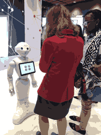 A white person with medium-length brown hair stands with their back to a camera in front of Aldebaran's Pepper, a humanoid robot on wheels.