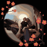 Two people crouch in front of a fisheye lens, smiling. A red flowering tree frame is around the photo.