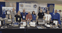 A group photo of 8 people standing behind a long table display covered in monitors and radio gadgets.